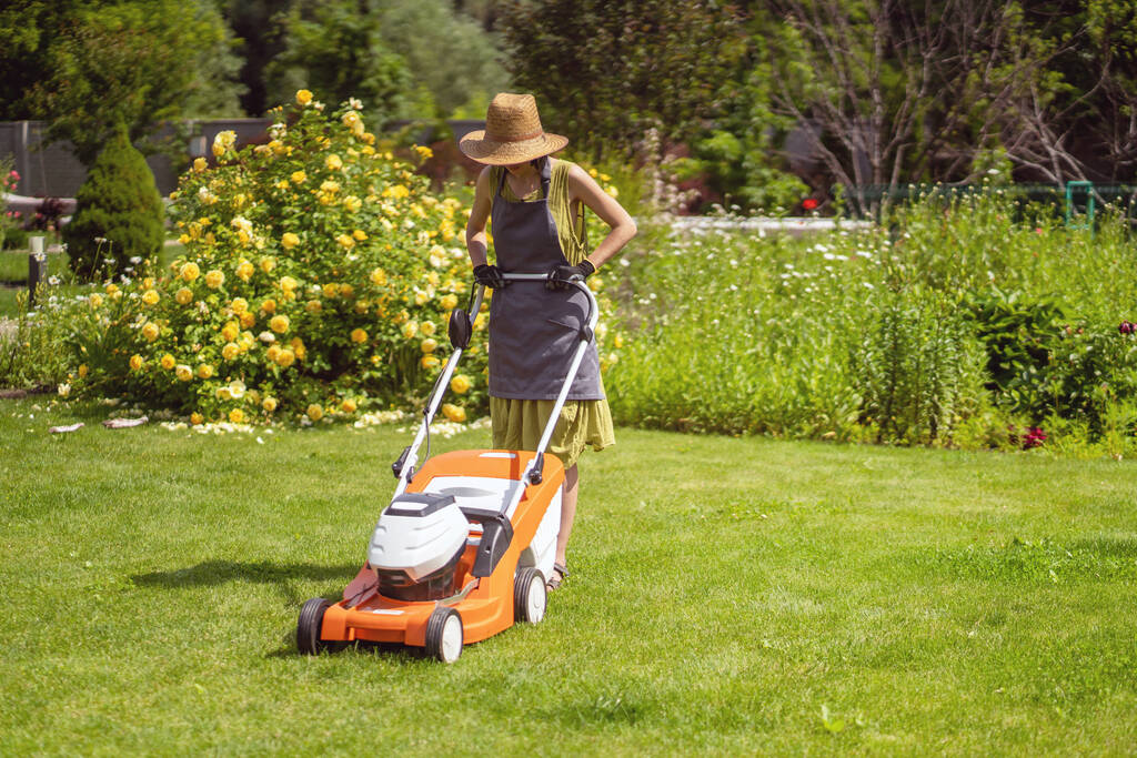 young girl in a straw hat is mowing a lawn
